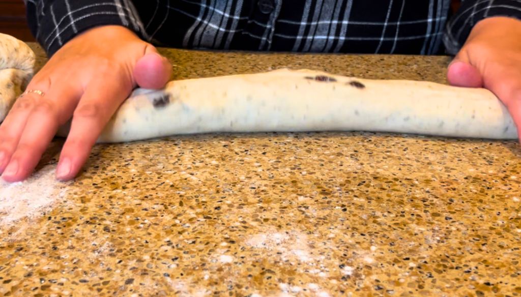 Woman rolling herb stuffing bread dough into a baguette shape