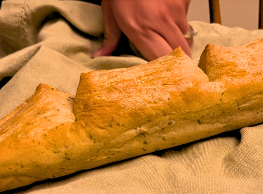 A baked herb stuffing baguette on a light green cloth and a woman's hand in the background