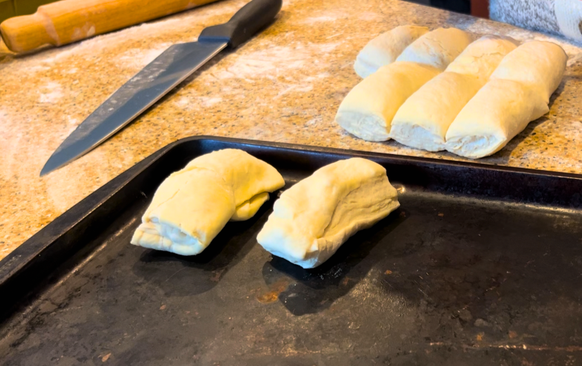 A woman splitting Scottish butter rolls into portions and placing them on a cookie sheet.