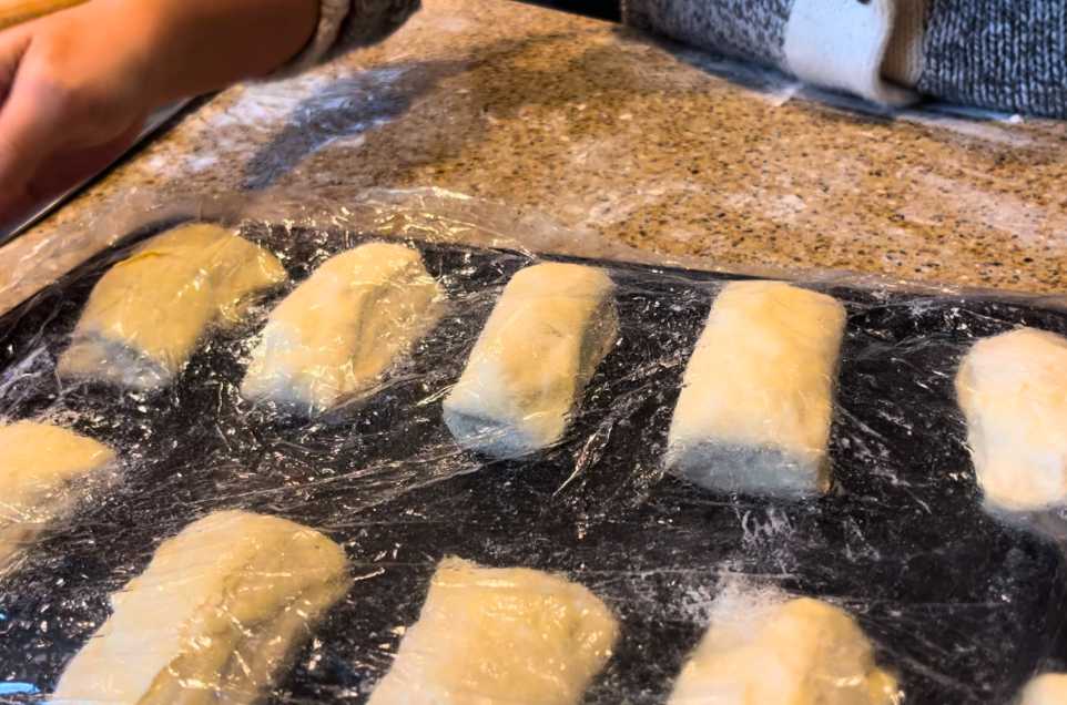 Scottish butter rolls rising on a cookie sheet. Covered with a layer of cling-film