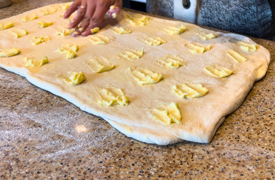 Scottish butter roll dough rolled into a rectangle with pats of butter on the top.