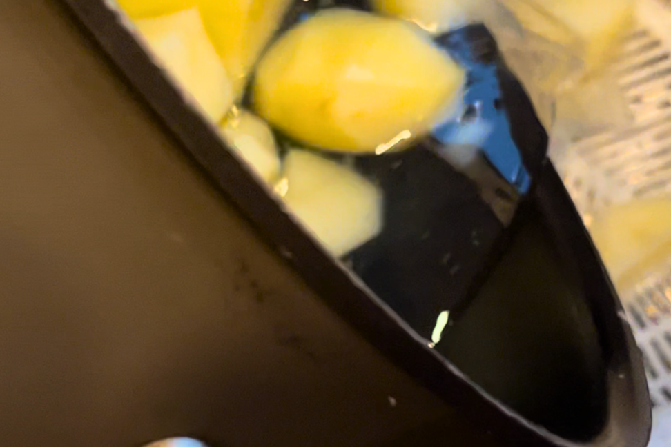 A large pot of peeled potatoes and water being poured into a colander.