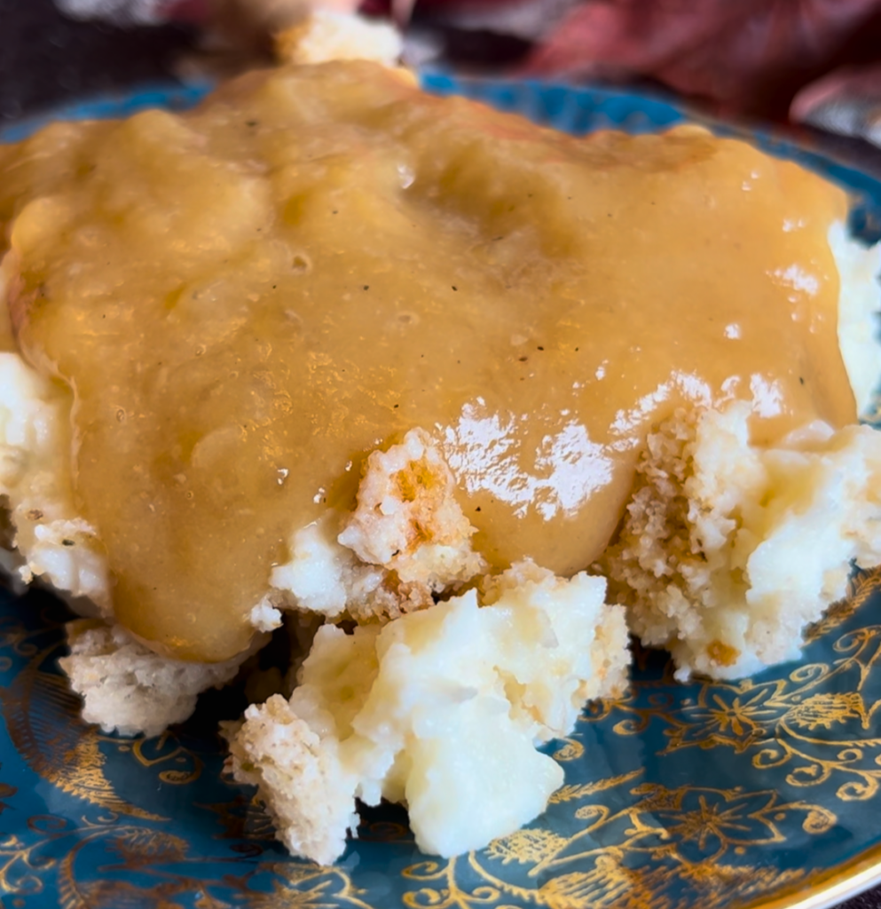 A blue and gold plate with mashed potato casserole and gravy on top.