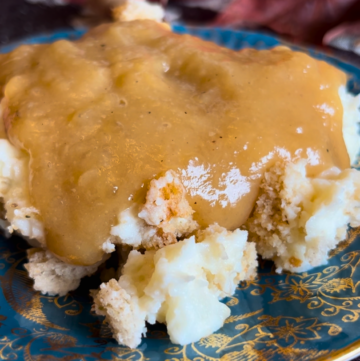 A blue and gold plate with mashed potato casserole and turkey gravy.