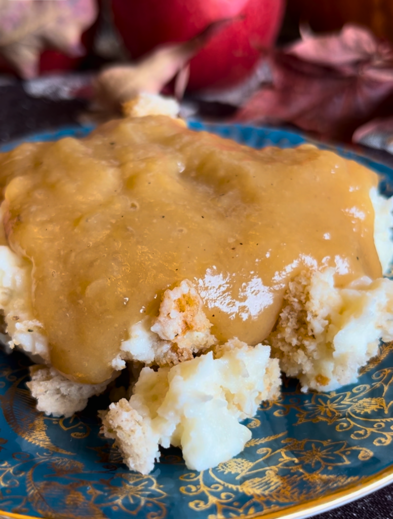 A blue and gold plate with mashed potato casserole and gravy.