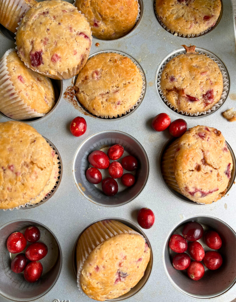 Cranberry muffins in a muffin tray with fresh cranberries around them