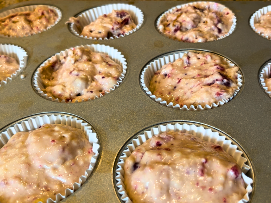 Muffin trays filled with cranberry muffin batter.