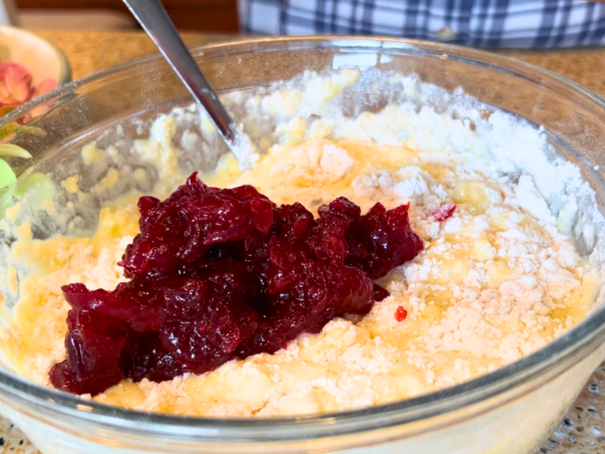 Woman adding cranberry sauce to muffin batter, in a glass bowl