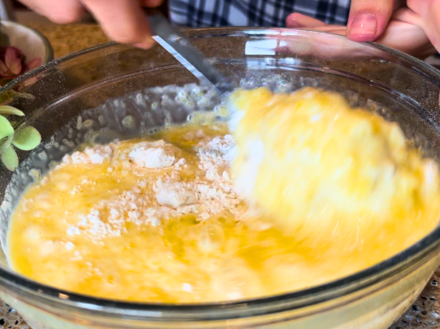 Woman gently mixing wet and dry ingredients together for muffin batter.