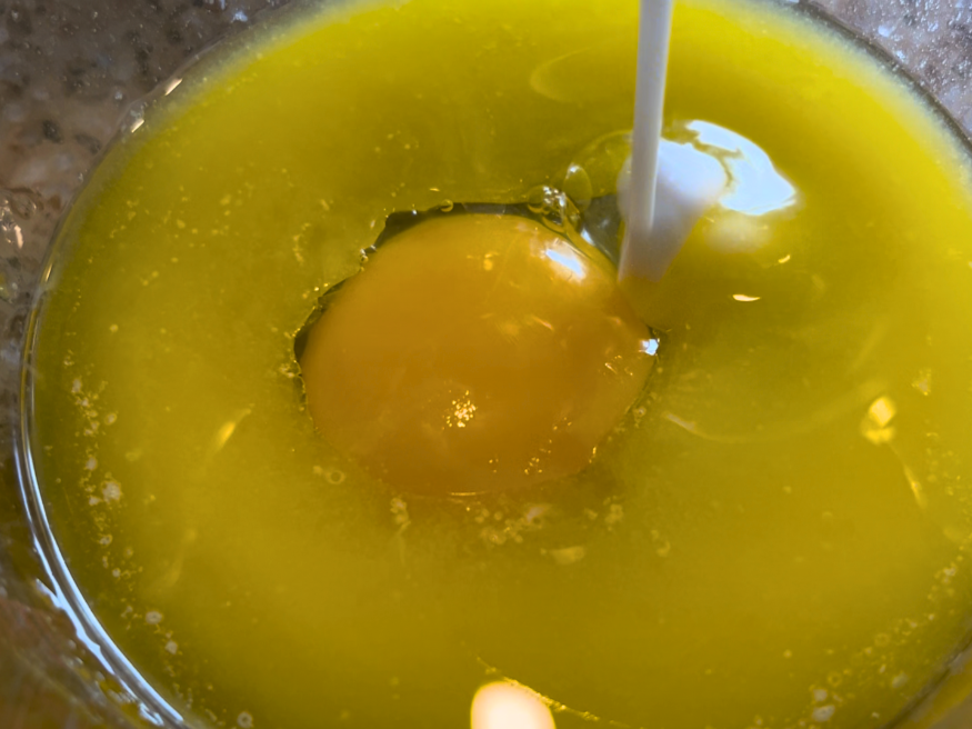 A glass measuring cup with melted butter, an egg, and milk being poured into it.