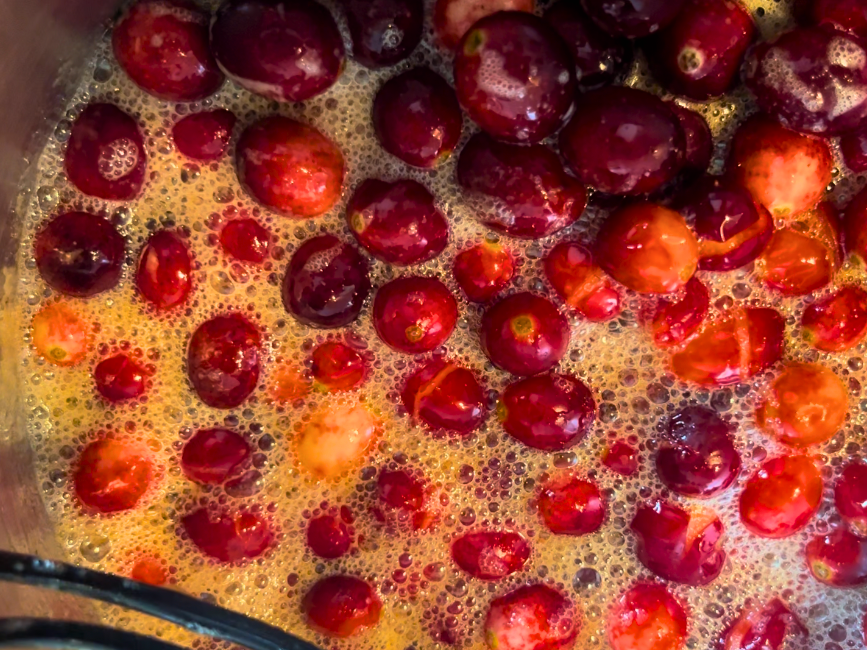 cranberries boiling in a sauce pot with sugar and cider.