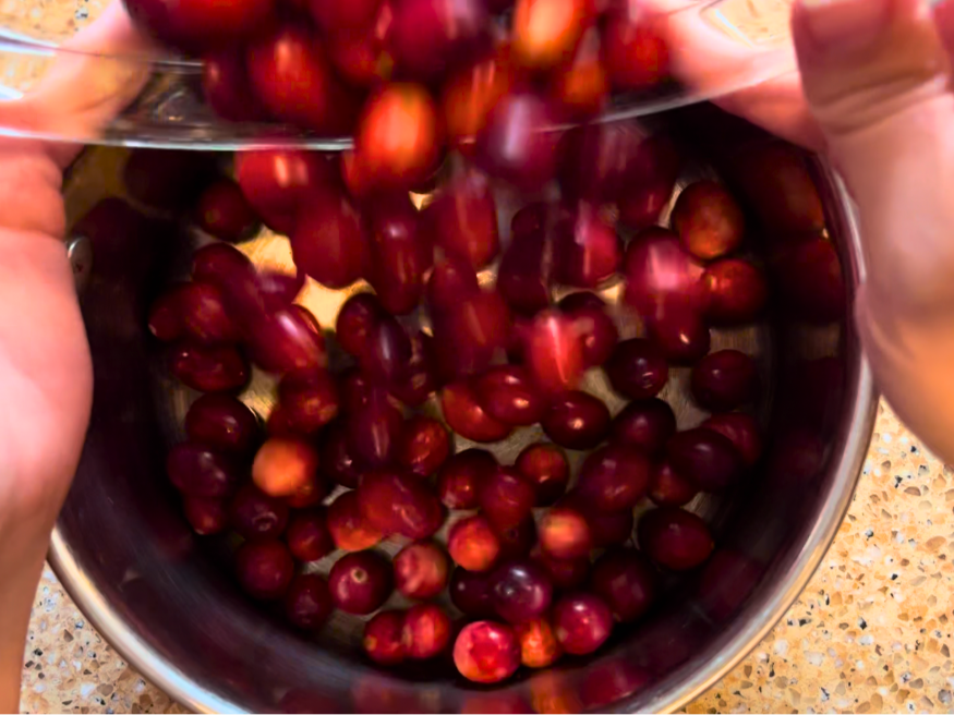 Woman pouring fresh cranberries from a glass bowl into a sauce pot.