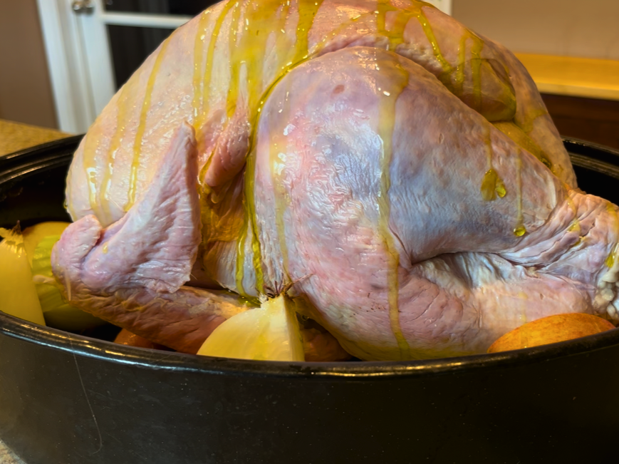 A woman drizzling oil on top of a turkey in a roasting pan