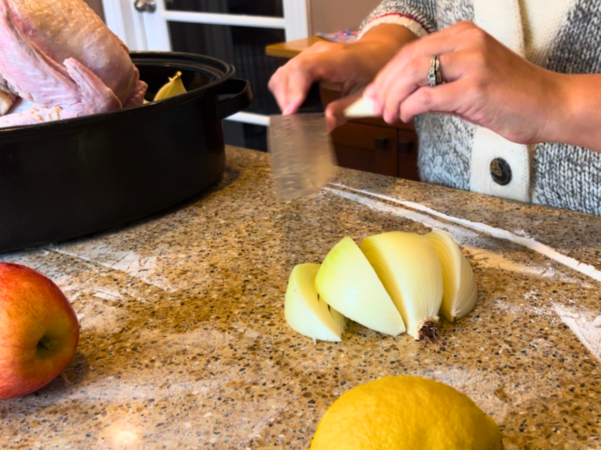 Woman cutting an onion into chunks a lemon in the foreground and a turkey in a roasting pan off to the side.