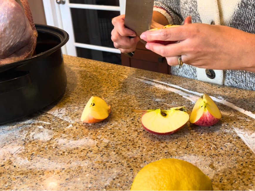 Woman cutting apples with a kitchen knife. A lemon in the foreground and a turkey in a roasting pan of to the side.