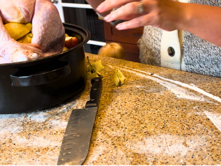 Woman adding lemons to a turkey in a roasting pan. A kitchen knife on the counter.