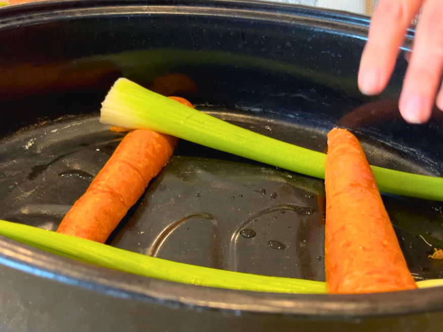 Celery ribs and carrot sticks forming a square in a black roasting pan.
