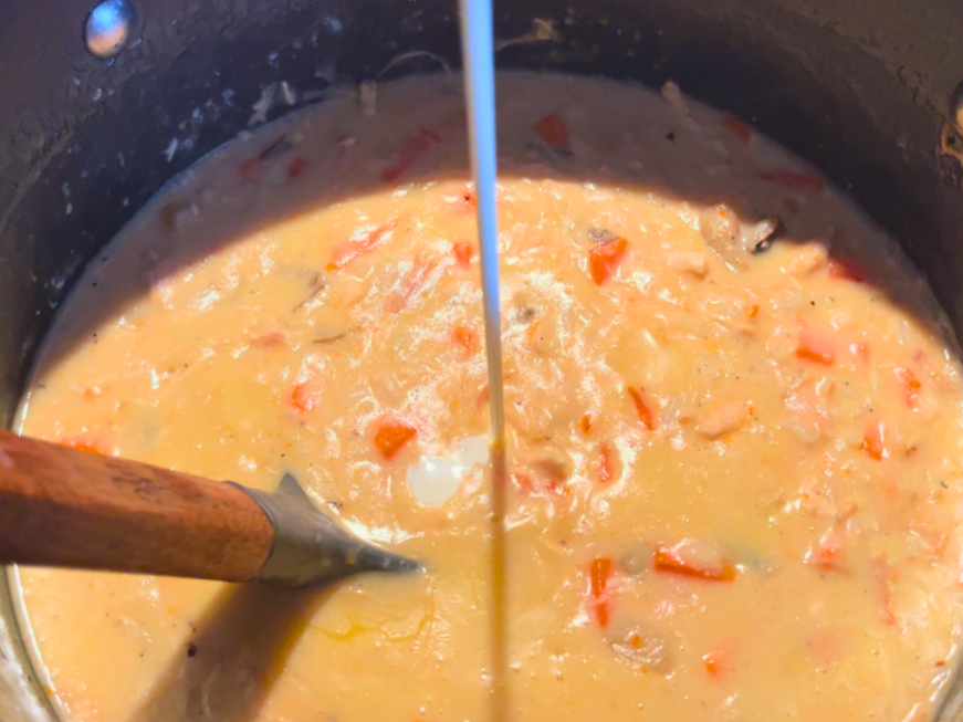 Pouring cream into a stockpot of creamy turkey and wild rice soup