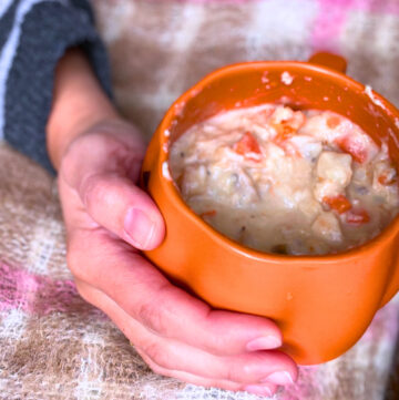 A woman holding a bowl of creamy turkey and wild rice soup in a pumpkin bowl.