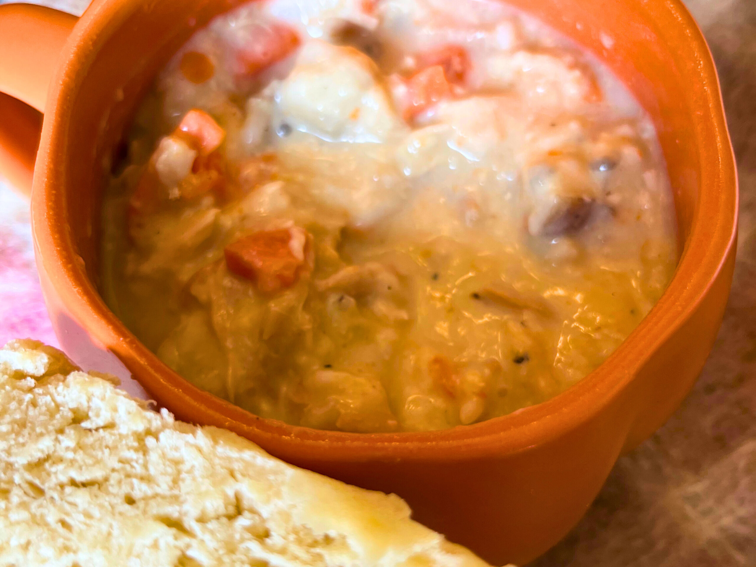 A bowl of creamy turkey and wild rice soup in a pumpkin mug. A sliced bun in the foreground