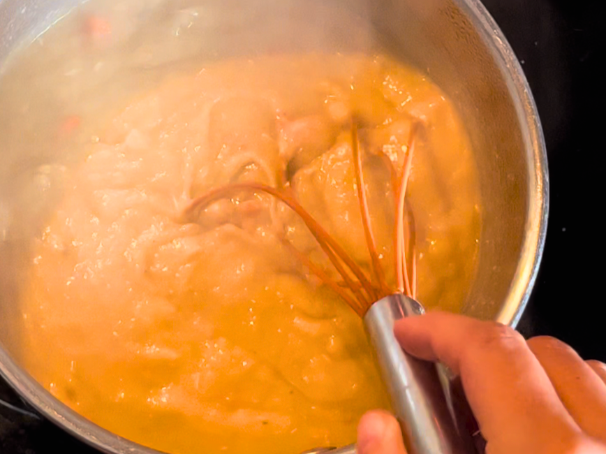 A thickened roux with turkey broth being stirred by a whisk