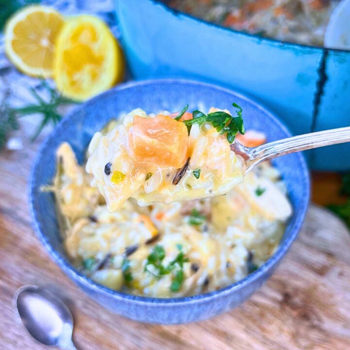 A blue bowl filled with turkey and rice soup. There is a blue pot in the background with more soup.