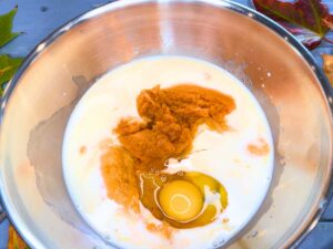 A metal bowl with milk, eggs, and pumpkin purée inside.