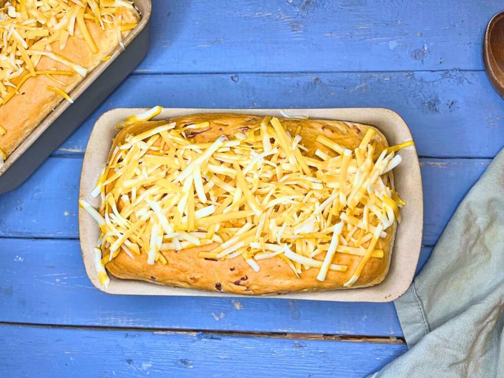 Baked cheese bread in a loaf pan with shredded cheese on top.