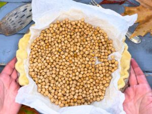 There is an unbaked pie crust with parchment paper and chickpeas inside.