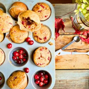 There is a muffin tin full of cranberry muffins. There are fresh cranberries in some of the cups.