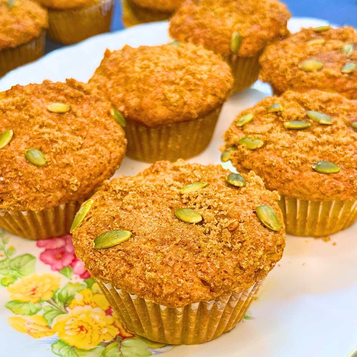 Six pumpkin muffins on a white floral plate.