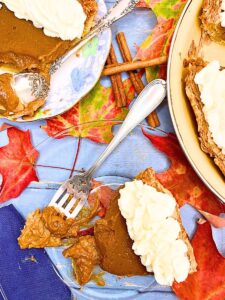 A piece of pumpkin pie with a bite out of it. There is the full pie off to the side.