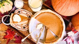 There is a pumpkin pie that has been sliced. sone slice is beside. There are pumpkins and leaves around.