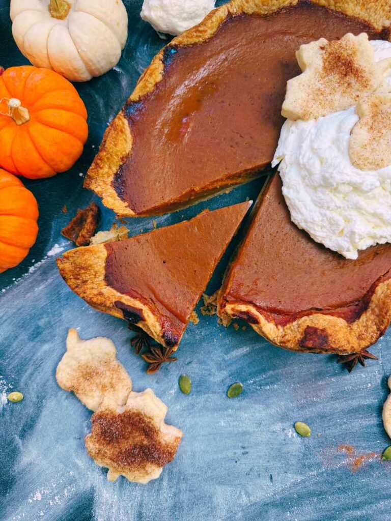 A sliced pumpkin pie with one slice cut. There is whipped cream on top.