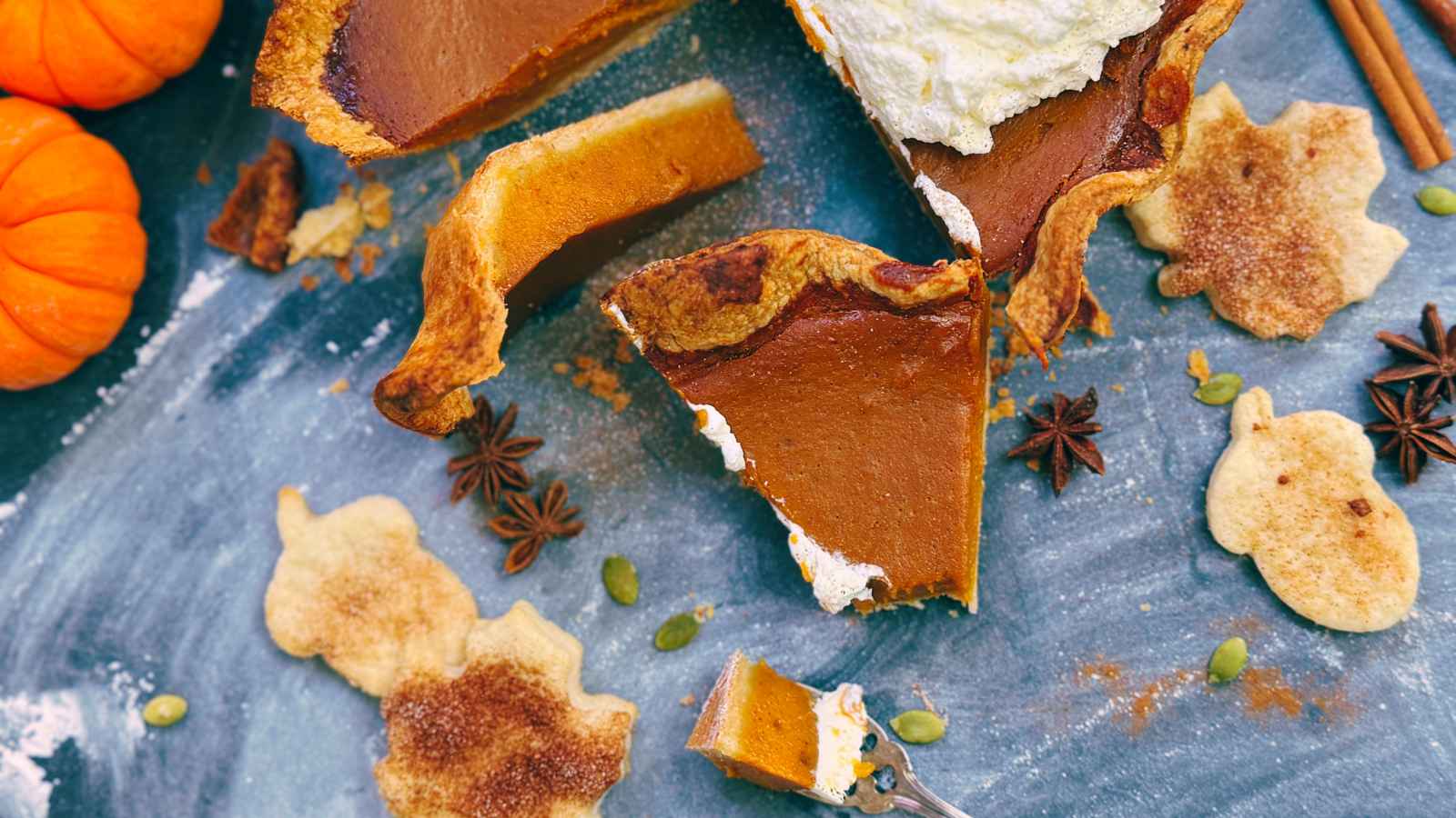 A sliced pumpkin pie with whipped cream on top. There are some small pumpkins in the background.