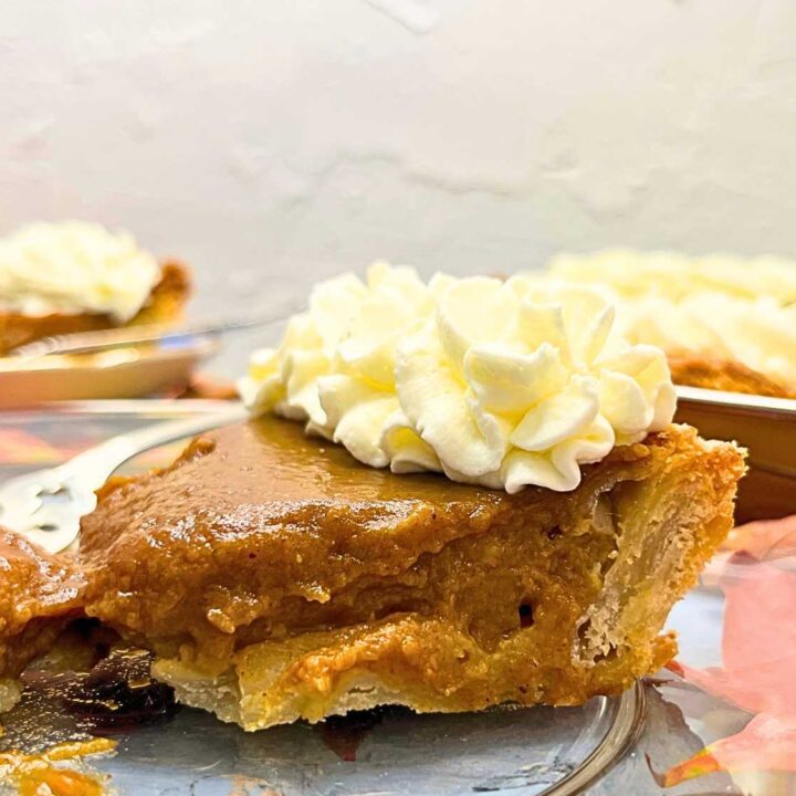 A side view of a pumpkin pie slice. There is whipped cream on top.