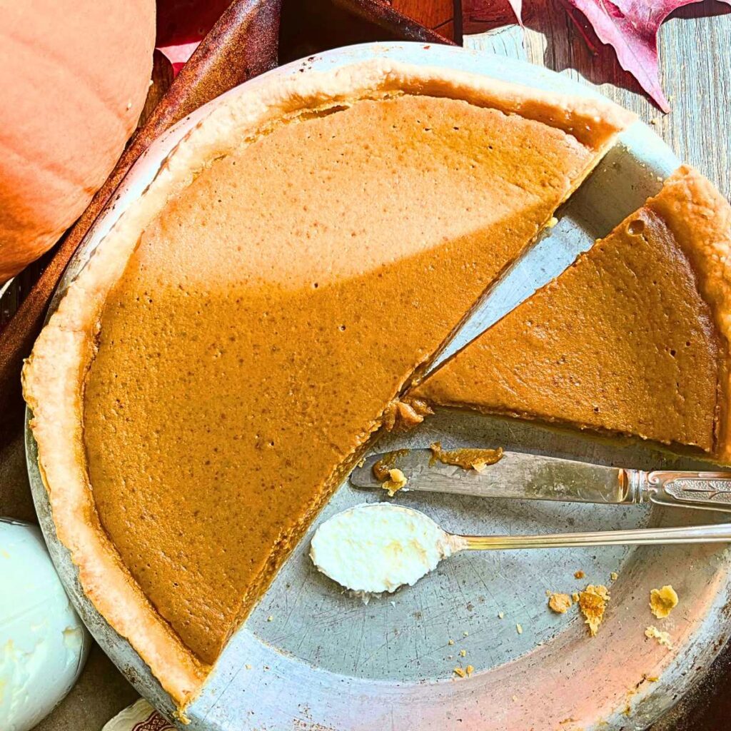 There is an overhead shot of a pumpkin pie that has been sliced and a piece is recmoved.