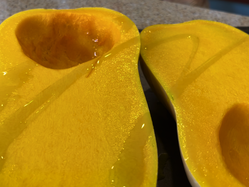 Two butternut squash halves with oil drizzled on top