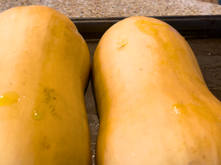 Two butternut squash halves on a cookie sheet with the skin side up.