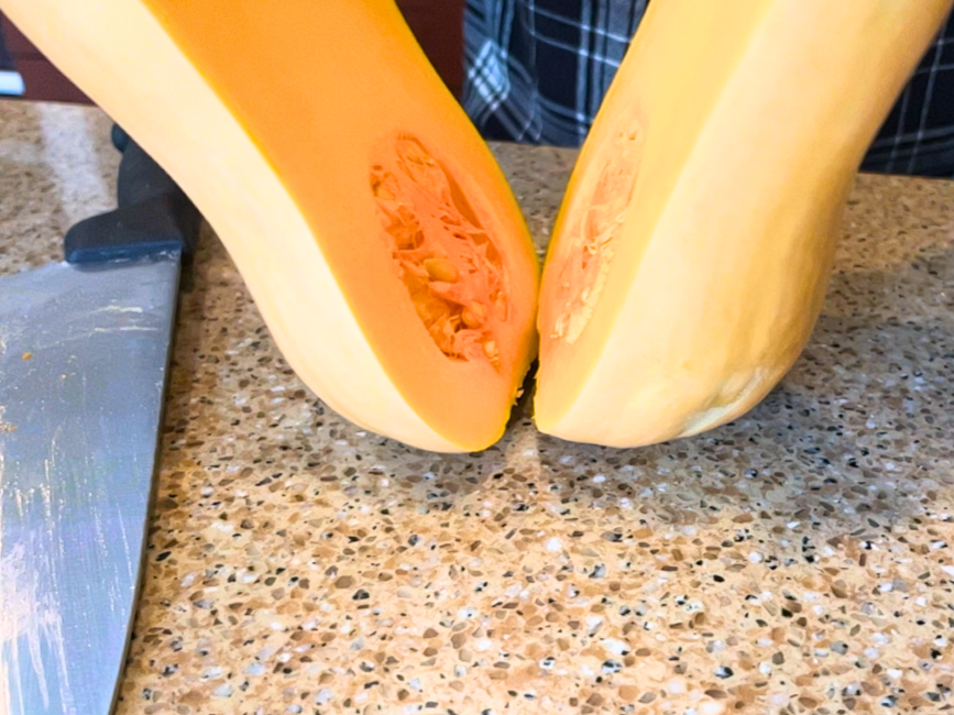 A butternut squash being cut length-wise by a woman.