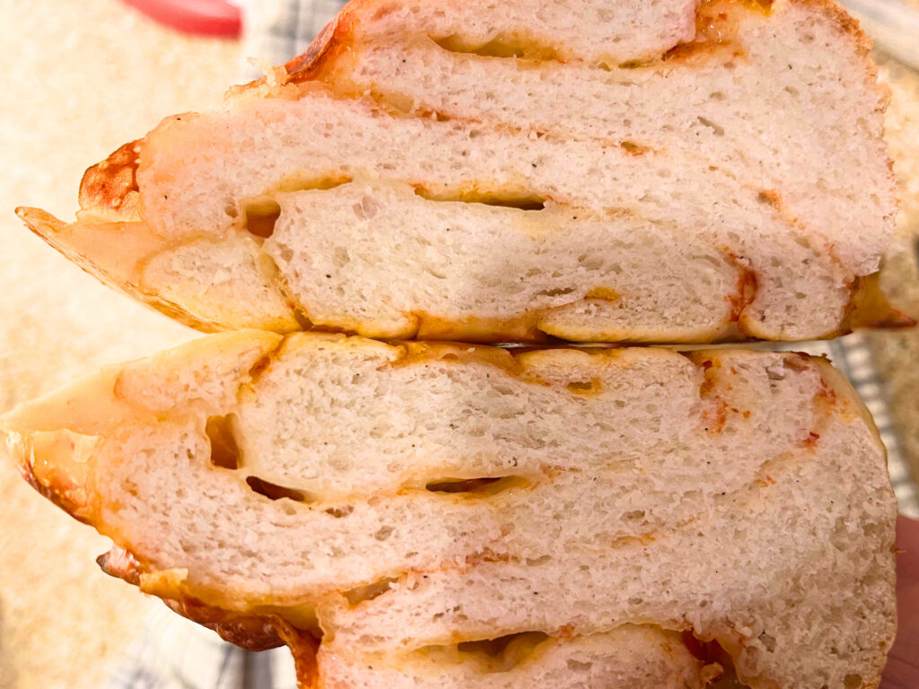 A cut cross section of a braided bread loaf, showing the swirls of pizza sauce and cheese.