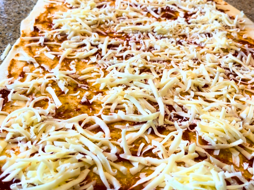 Bread dough with pizza sauce and grated mozzarella cheese spread on top.