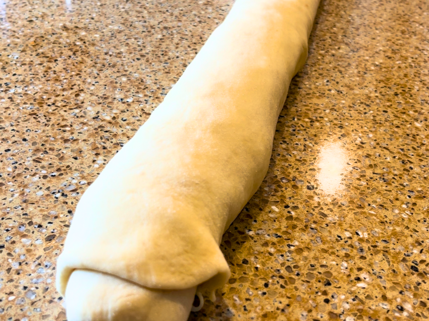 Bread dough rolled into a log shape on a brown counter top.