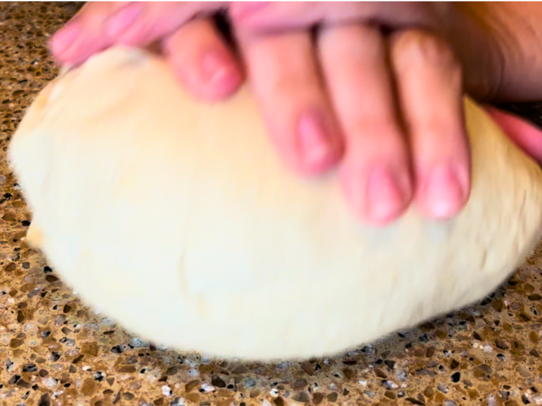 A woman kneading bread dough on a brown counter top.
