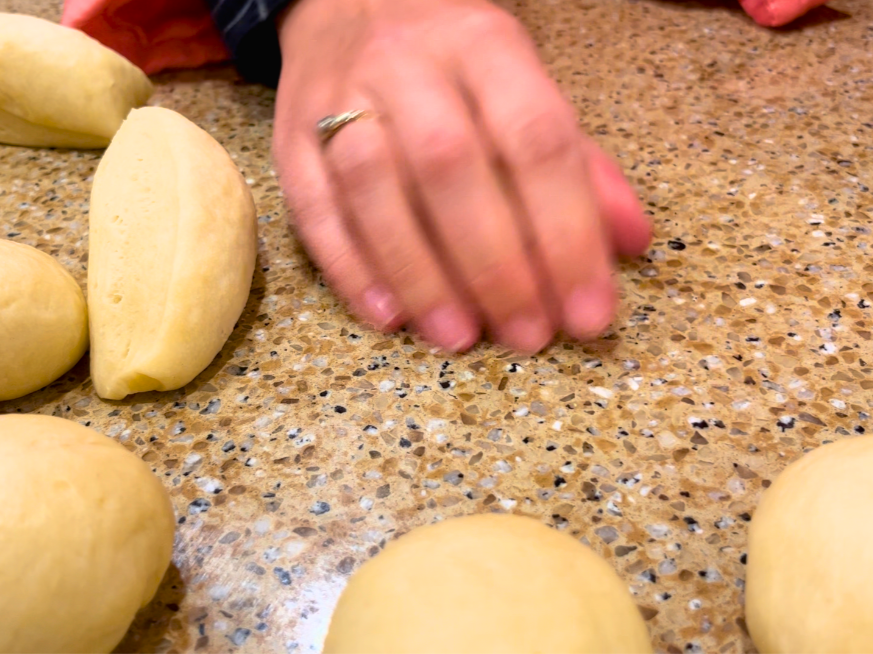 woman rolling dinner roll dough on a counter to make a sphere shape