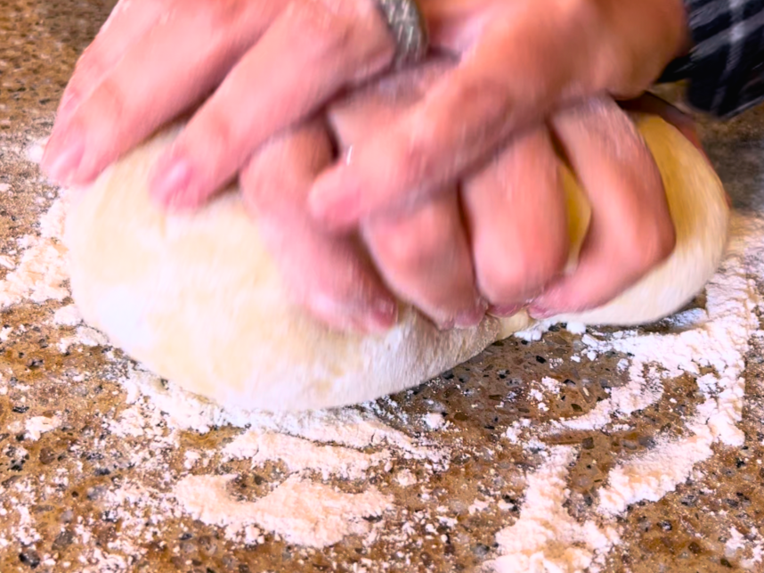 Woman kneading dinner roll dough on a floured counter top.