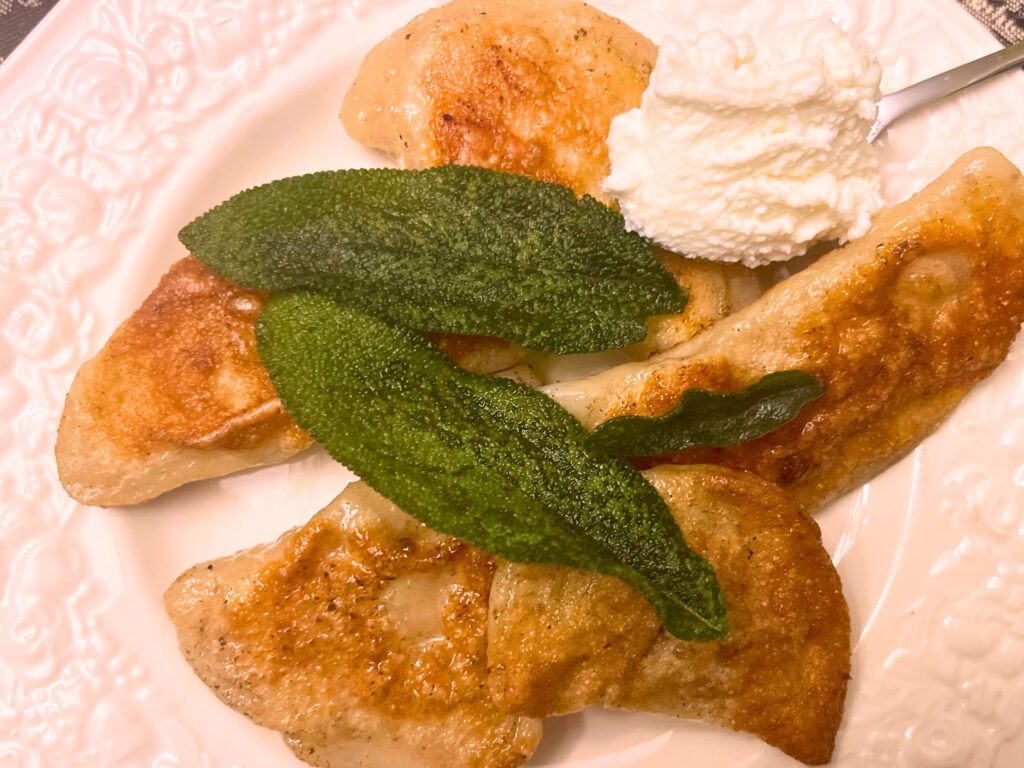 A plate of pierogies with fried sage leaves and cream cheese on the side