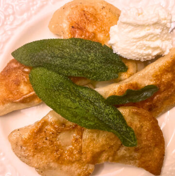 A plate of pierogies with fried sage leaves and cream cheese on the side