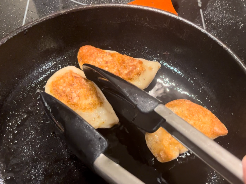 Woman turning pierogies that are frying in a pan with butter