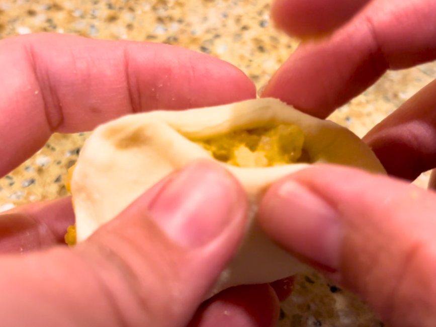Woman pinching the sides of the dough around the pierogi filling